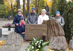 Dwie panie, jeden pan i dwie dziewczynki stoją za grobem, przed nimi widoczna kamienna tablica z krzyżem i napisem Jan Witold Moll.