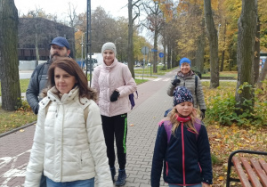 Dwie panie, jeden pan i dwie dziewczynki idą ulicą wzdłuż parku, w oddali za nimi budynek Orientarium.