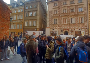 Grupa uczniów klasy 8c i 8a stojąca przed zabytkowym kościołem na Starym Mieście, odpowiadająca na pytania pani przewodnik.