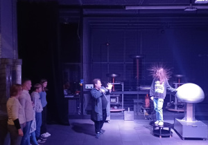 Eksperyment fizyczny na terenie Centrum nauki Kopernik, prezentujący uczennicę, której wskutek doświadczenia fizycznego włosy stanęły dęba.