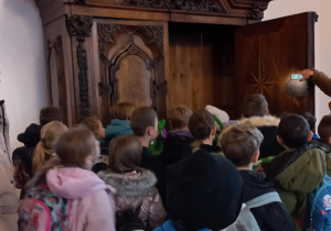 Uczniowie zwiedzają zamek wraz z przewodniczką, która opowiada im historii i tradycjach.