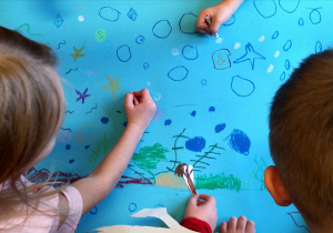 Dzieci wykonujące rysunek na niebieskim kartonie.