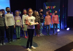 Zwyciężczyni konkursu "Spring is coming" stojąca na scenie z dziećmi ze swojej klasy.