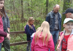 Pięć dziewczynek i trzech tatusiów stoją na pomoście w podmokłym lesie.