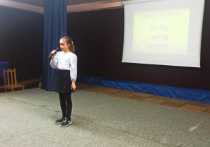 Dziewczynka stoi na scenie trzymając w dłoni mikrofon recytuje wierszyk.