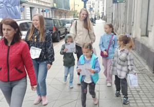 Trzy kobiety i cztery dziewczynki idą ulicą, dziewczynki w rękach trzymają mapki.