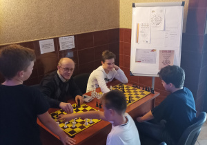 Czterech chłopców grających w szachy z panem Krzysztofem Zgołą- opiekunem koła szachowego.