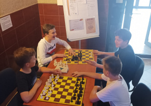 Czterech chłopców grających w szachy przy wejściu głównym do szkoły.