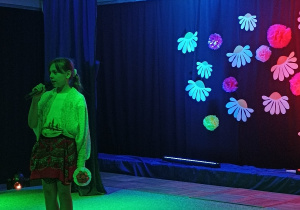 Dziewczynka stojąca na scenie i recytująca wiersz przez mikrofon.