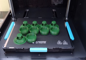 Upominek. Na stole roboczym drukarki 3D leży pięć wydrukowanych zabawek typu Fidget składających się z dwóch elementów każda.