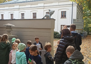 Grupa dzieci i dwoje dorosłych patrzących na figurkę Kota Filemona na murze przy wejściu do Muzeum Kinematografii.