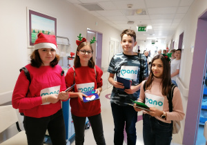 Dzieci ubrane świątecznie w holu szpitalnym trzymają kartki bożonarodzeniowe.