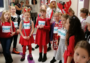 Dzieci ubrane świątecznie w holu szpitalnym śpiewają kolędy.