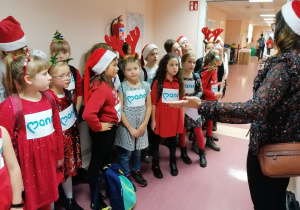 Dzieci ubrane świątecznie w holu szpitalnym śpiewają kolędy.