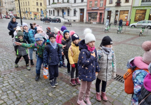 Dzieci słuchające przewodnika opowiadającego o Toruniu.