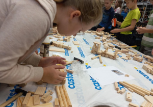 Dzieci w skupieniu składają drewniany pojazd.