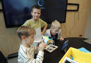 3 osobowa grupka chłopców konstruuje z klocków zabawkę robota.