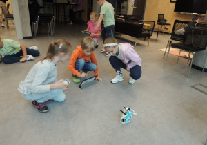 Dzieci w trzyosobowych grupkach programują swoje roboty z wykorzystaniem tabletów.