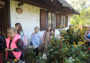 Dziewczynki stoją w ogródku przed chatą.