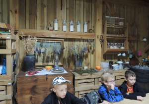 Chłopcy siedzą przy drewnianych stołach, w tle rozwieszone są na sznurkach suszone zioła.