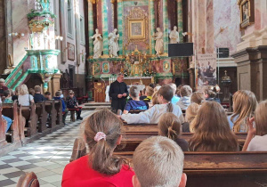 Uczniowie znajdują się we wnętrzu Bazyliki w Studziannie-Poświętnem i słuchają opowieści księdza proboszcza.