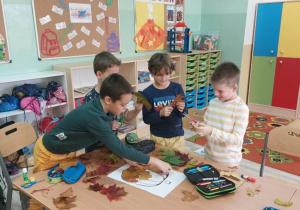 Uczniowie w grupach wyklejają liśćmi kontur dyni.