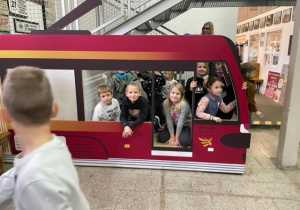 W czerwonym modelu tramwaju grupa dzieci pozuje do zdjęcia.