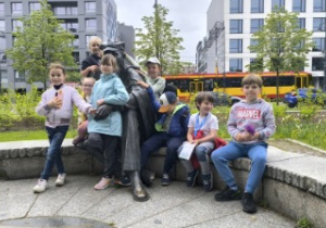Przy pomniku harcmistra Aleksandra Kamińskiego siedząc na murku dzieci pozują do zdjęcia .