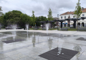 Zdjęcie przedstawia Plac Staromiejski, na którym znajdują się liczne fontanny. Wokól nich ustawione są ławeczki.