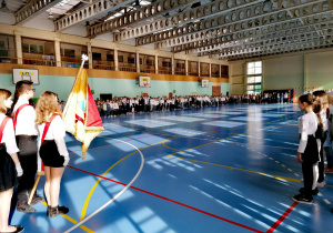 Uczniowie ubrani na galowo śpiewają hymn w sali gimnastycznej.