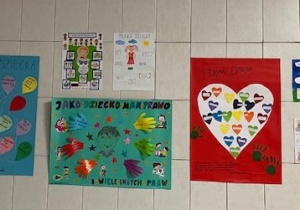 Osiem plakatów różnej wielkości wisi na ścianie wyłożonej jasnymi płytkami. Są to plakaty z balonikami, sercami, zdjęciami, rysunkami i napisami mówiącymi o prawach dzieci. Prace są kolorowe i estetycznie wykonane.