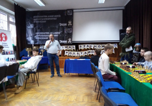 Sala turniejowa, przez mikrofon mówi organizator turnieju mistrz szachowy Sylwester Bednarek.