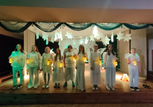 Widok na całą scenę, na której stoją uczniowie przebrani za anioły - każdy z nich trzyma w ręku mały biały lampion