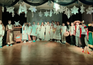 Widok na całą scenę, na której stoją wszyscy aktorzy jasełek w przebraniach, w tle widać stajenkę.