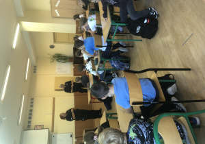 Spotkanie w sali. Dzieci siedzą w ławkach. Funkcjonariusze stoją przed nimi.