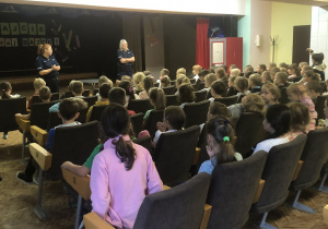 Spotkanie  sali widowiskowej. Funkcjonariusze stoja przed siedzącymi uczniami. Przekazuja wiedzę.