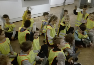 Dzieci w kamizelkach odblaskowych siedzące w holu muzeum.