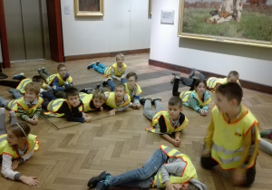 Dzieci w kamizelkach odblaskowych leżące w holu muzeum.
