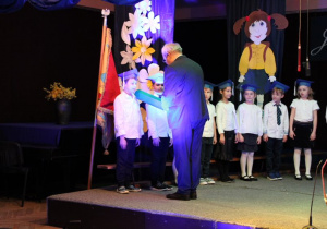 Pan Dyrektor pasuje dzieci na uczniów, nakładając na ich ramię duży granatowy ołówek.